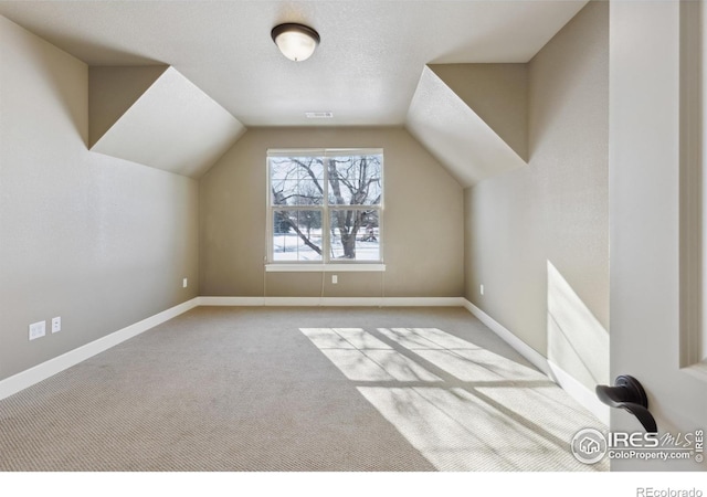 additional living space featuring light carpet, vaulted ceiling, and a textured ceiling