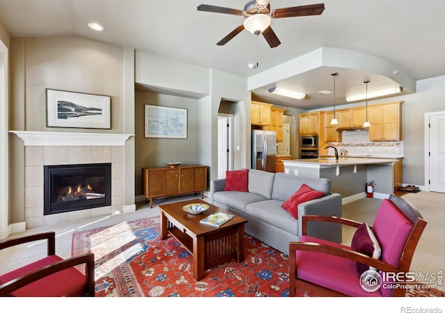 carpeted living room with lofted ceiling, ceiling fan, sink, and a tiled fireplace