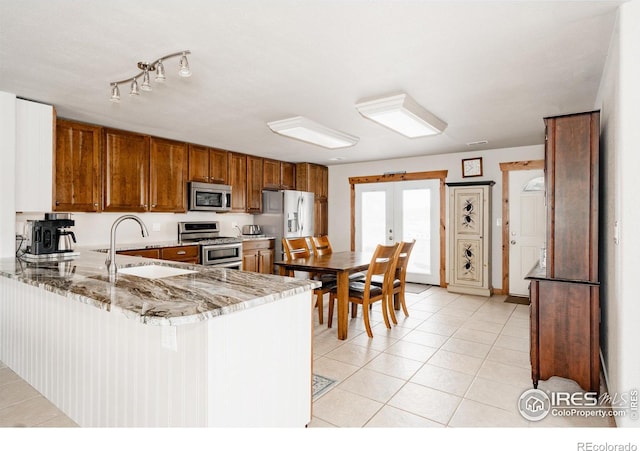 kitchen with light tile patterned floors, brown cabinets, a peninsula, stainless steel appliances, and a sink