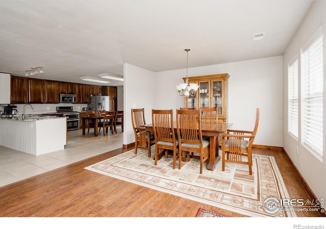 dining room with a notable chandelier, light wood-style flooring, visible vents, and baseboards