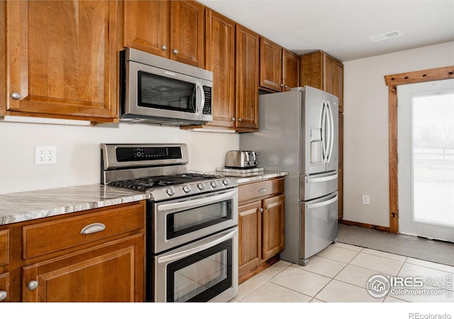 kitchen featuring stainless steel appliances, light tile patterned flooring, visible vents, and brown cabinets