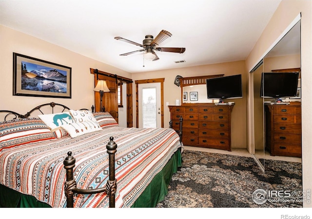 carpeted bedroom with a barn door, a closet, visible vents, and a ceiling fan