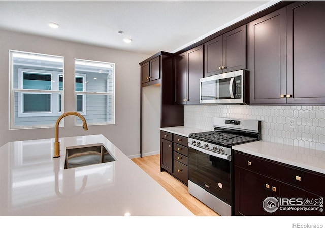 kitchen featuring sink, appliances with stainless steel finishes, dark brown cabinetry, decorative backsplash, and light wood-type flooring