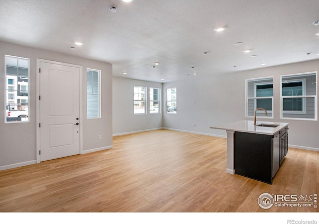 kitchen with sink, a center island with sink, a textured ceiling, and light wood-type flooring