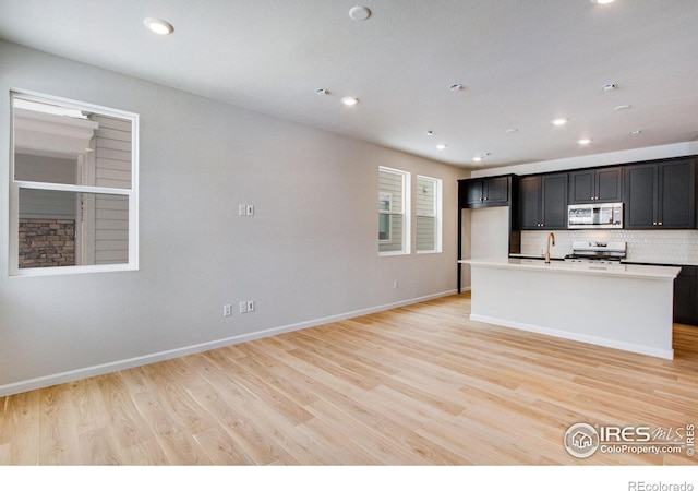 kitchen with tasteful backsplash, stainless steel appliances, a center island with sink, and light wood-type flooring