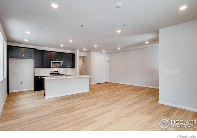 kitchen featuring sink, decorative backsplash, a kitchen island with sink, light hardwood / wood-style floors, and stainless steel appliances