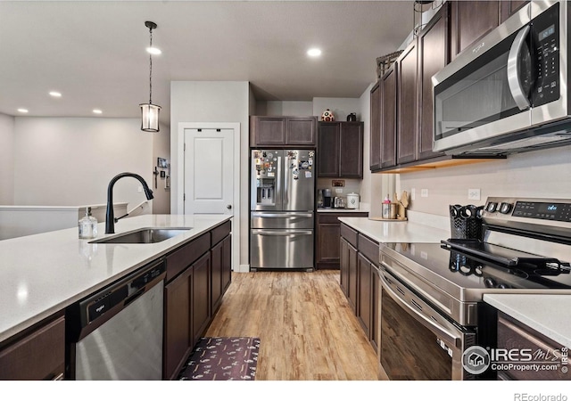 kitchen featuring dark brown cabinetry, sink, pendant lighting, stainless steel appliances, and light hardwood / wood-style floors