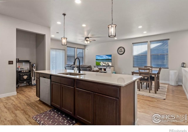 kitchen with decorative light fixtures, an island with sink, sink, stainless steel dishwasher, and light hardwood / wood-style flooring