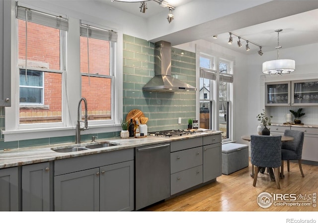 kitchen with wall chimney range hood, sink, appliances with stainless steel finishes, gray cabinetry, and decorative light fixtures