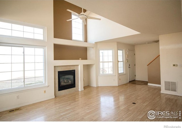 unfurnished living room featuring ceiling fan, plenty of natural light, a fireplace, and light hardwood / wood-style flooring