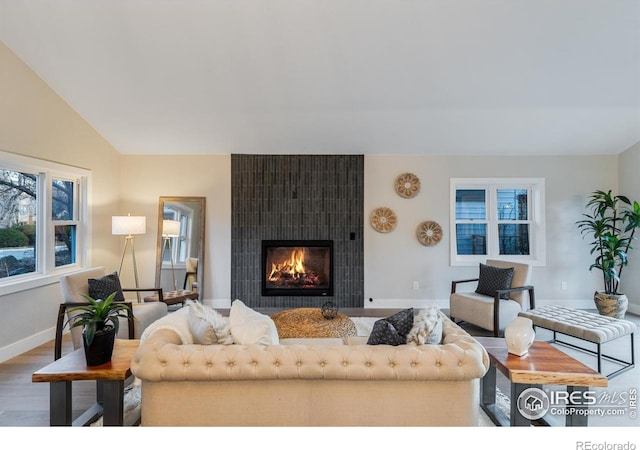 living room featuring a tiled fireplace, wood-type flooring, and vaulted ceiling