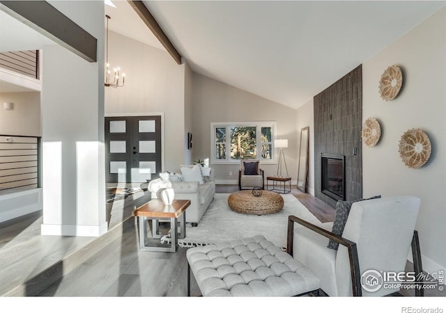 living room featuring a tile fireplace, high vaulted ceiling, beamed ceiling, light wood-type flooring, and an inviting chandelier