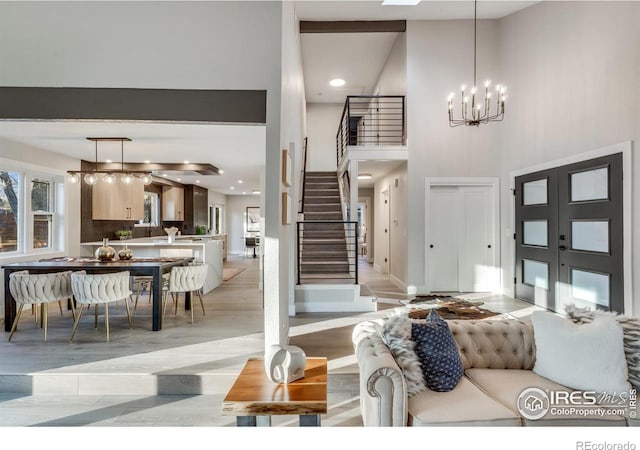 living room with french doors, a towering ceiling, a chandelier, and light hardwood / wood-style flooring