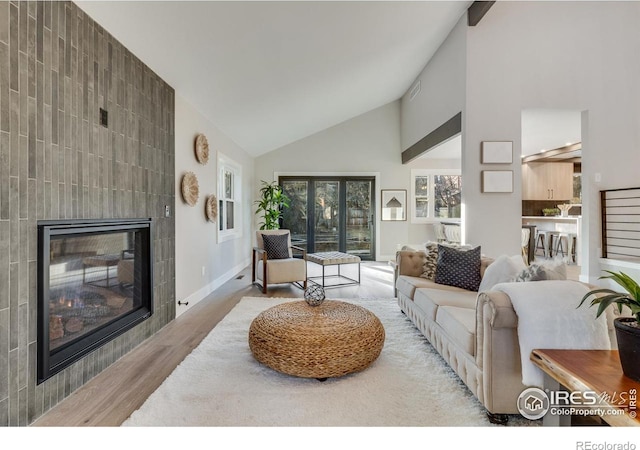 living room featuring high vaulted ceiling, a tile fireplace, and light wood-type flooring