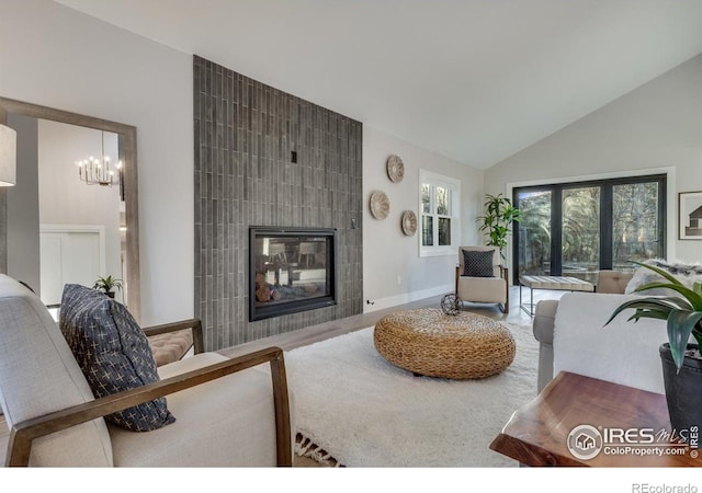 living room with a tiled fireplace, hardwood / wood-style floors, lofted ceiling, and a chandelier