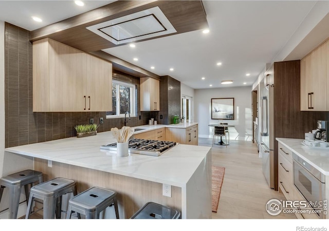 kitchen with light brown cabinetry, a breakfast bar area, light stone counters, kitchen peninsula, and decorative backsplash