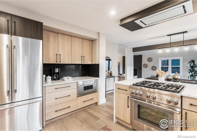 kitchen with light hardwood / wood-style flooring, hanging light fixtures, tasteful backsplash, premium appliances, and light brown cabinets