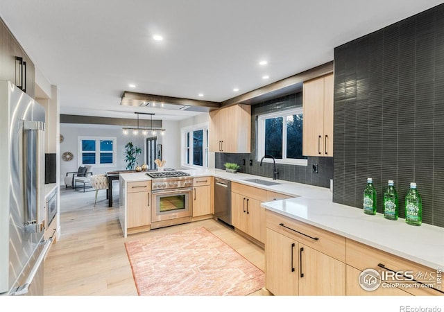 kitchen with light brown cabinetry, sink, appliances with stainless steel finishes, kitchen peninsula, and pendant lighting