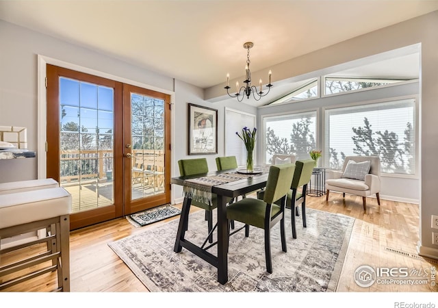 dining space with french doors, vaulted ceiling, a chandelier, and light hardwood / wood-style flooring