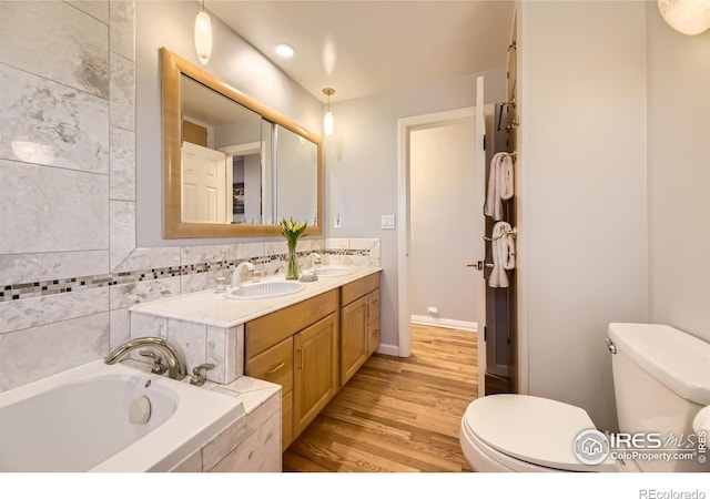 bathroom with toilet, tasteful backsplash, wood-type flooring, vanity, and a relaxing tiled tub