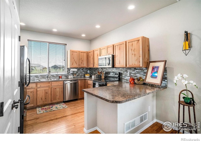 kitchen with visible vents, a peninsula, light wood-type flooring, tasteful backsplash, and stainless steel appliances