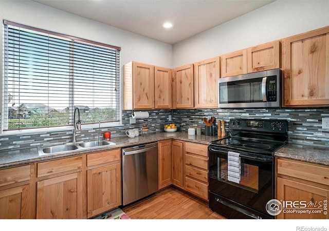 kitchen with a sink, appliances with stainless steel finishes, decorative backsplash, and light wood-type flooring