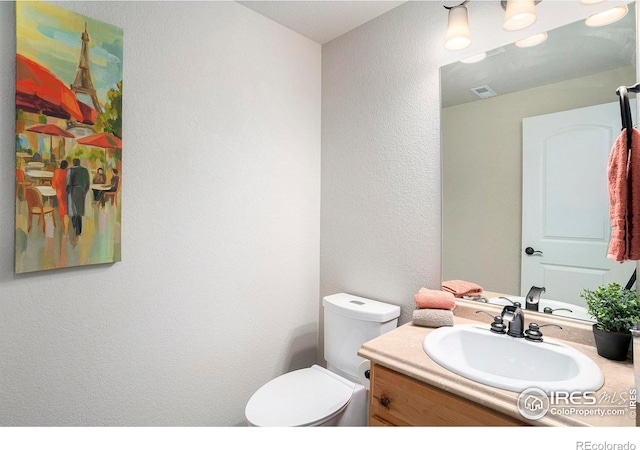 half bath featuring toilet, a textured wall, visible vents, and vanity