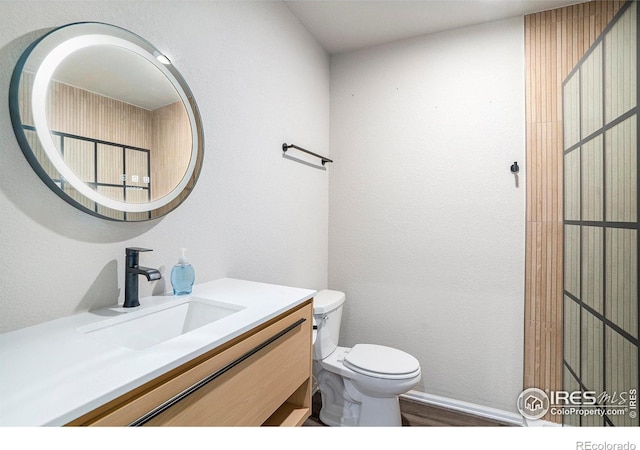half bathroom with vanity, baseboards, toilet, and wood finished floors