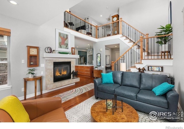 living room with a tiled fireplace, a high ceiling, and hardwood / wood-style floors