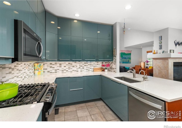 kitchen with appliances with stainless steel finishes, sink, decorative backsplash, a tiled fireplace, and kitchen peninsula