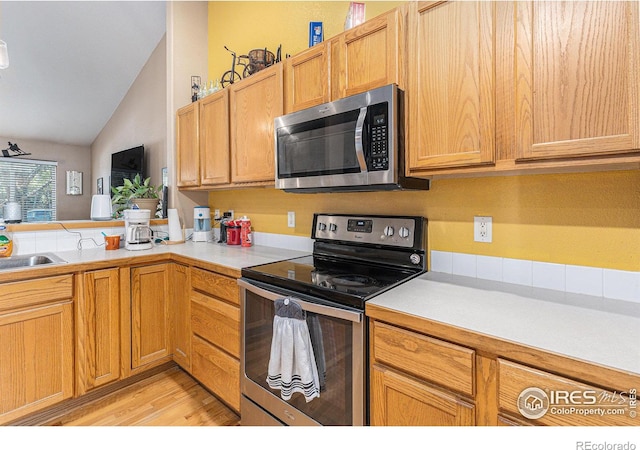 kitchen featuring light hardwood / wood-style flooring, vaulted ceiling, kitchen peninsula, and appliances with stainless steel finishes