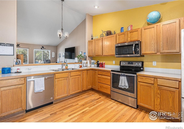 kitchen featuring appliances with stainless steel finishes, decorative light fixtures, lofted ceiling, sink, and light hardwood / wood-style flooring