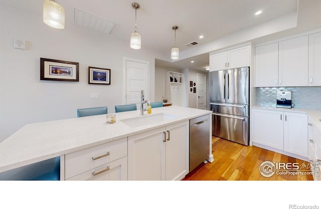 kitchen with sink, decorative light fixtures, stainless steel appliances, light stone countertops, and white cabinets