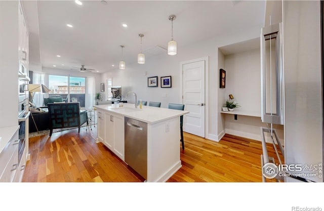 kitchen featuring sink, appliances with stainless steel finishes, a kitchen island with sink, white cabinets, and decorative light fixtures