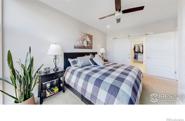 bedroom featuring a walk in closet, a barn door, light carpet, and ceiling fan