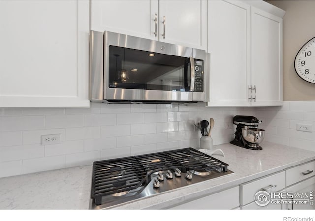 kitchen featuring white cabinetry, stainless steel appliances, light stone counters, and backsplash