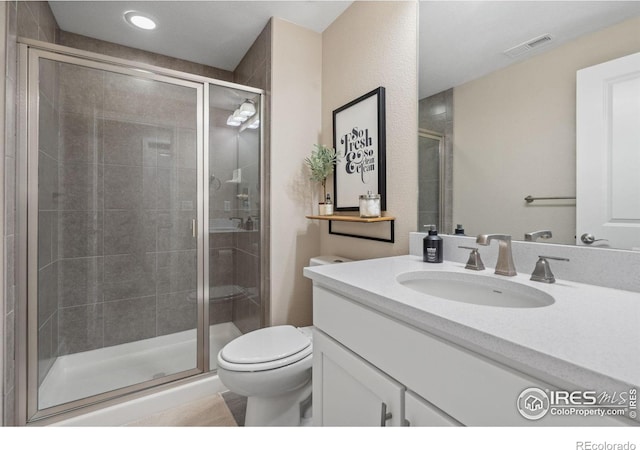 bathroom featuring a shower with door, vanity, and toilet