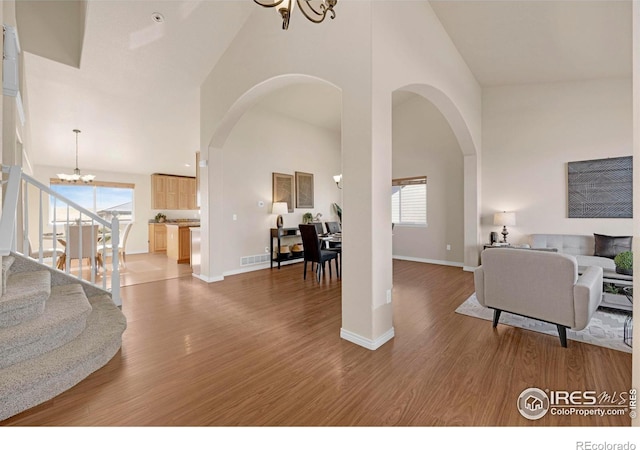 living area featuring arched walkways, a towering ceiling, wood finished floors, a healthy amount of sunlight, and a chandelier