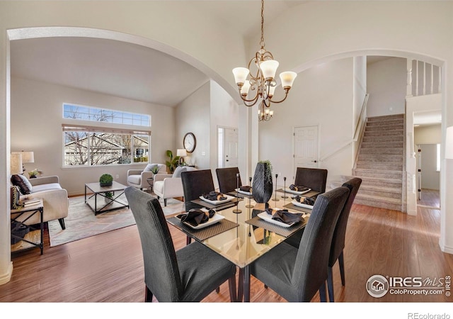 dining area featuring high vaulted ceiling, a notable chandelier, stairway, and wood finished floors