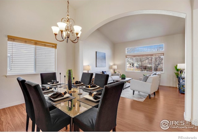 dining room with arched walkways, vaulted ceiling, baseboards, and light wood-style floors