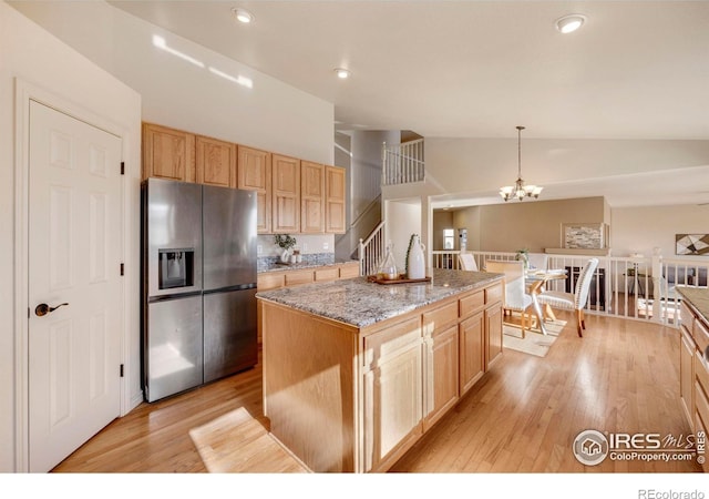 kitchen with light stone counters, a kitchen island, light wood-style floors, stainless steel refrigerator with ice dispenser, and pendant lighting