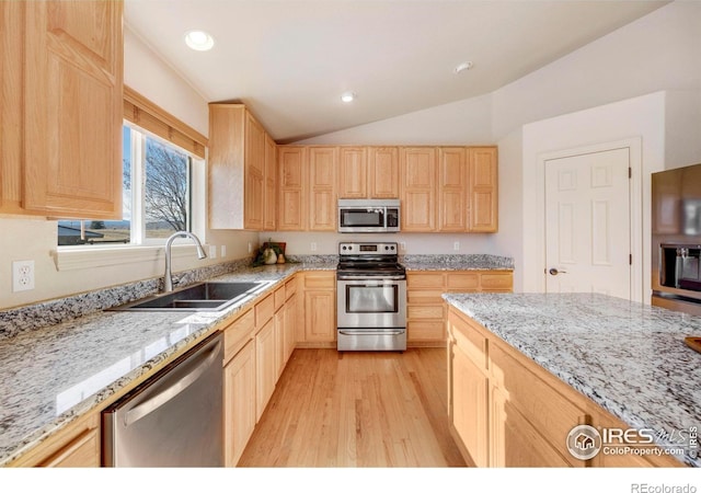 kitchen with light stone counters, a sink, vaulted ceiling, appliances with stainless steel finishes, and light brown cabinetry