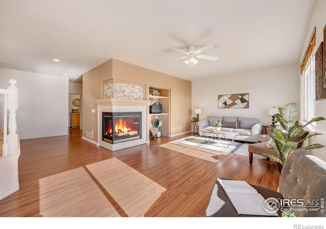 living area featuring a fireplace, visible vents, ceiling fan, wood finished floors, and baseboards