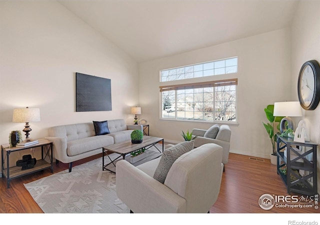 living area featuring high vaulted ceiling, visible vents, baseboards, and wood finished floors