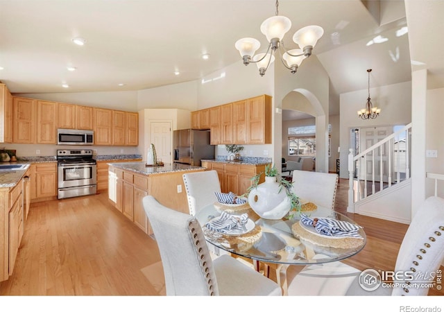 kitchen with a center island with sink, light stone countertops, an inviting chandelier, stainless steel appliances, and pendant lighting