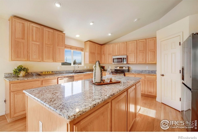 kitchen featuring appliances with stainless steel finishes, a center island, light brown cabinets, and a sink