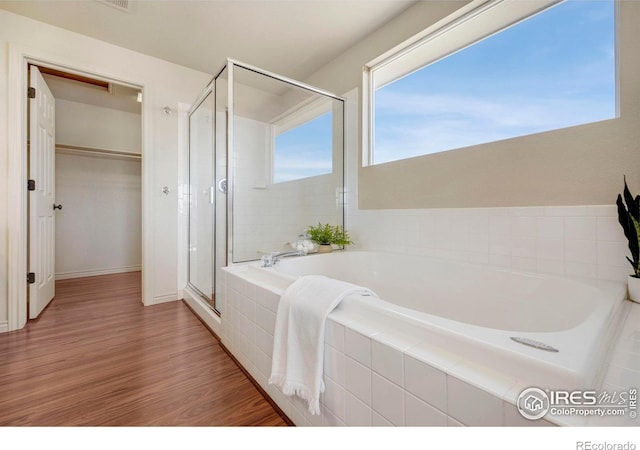 full bath featuring a stall shower, a walk in closet, a bath, and wood finished floors