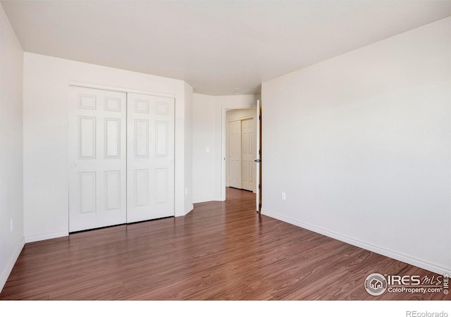 unfurnished bedroom with a closet, dark wood finished floors, and baseboards