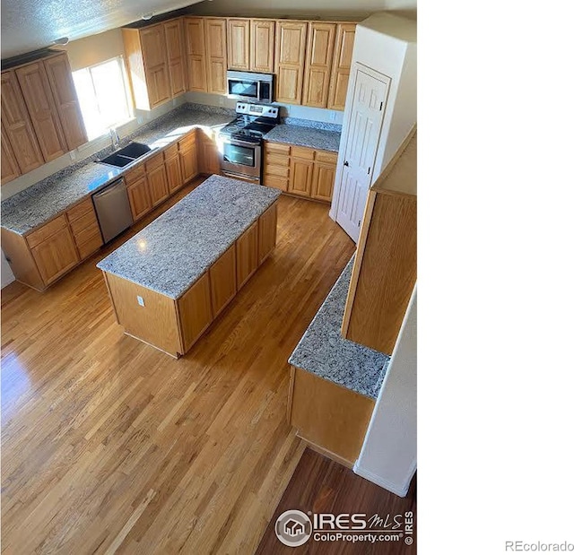 kitchen featuring brown cabinetry, light wood-style flooring, appliances with stainless steel finishes, a center island, and a sink