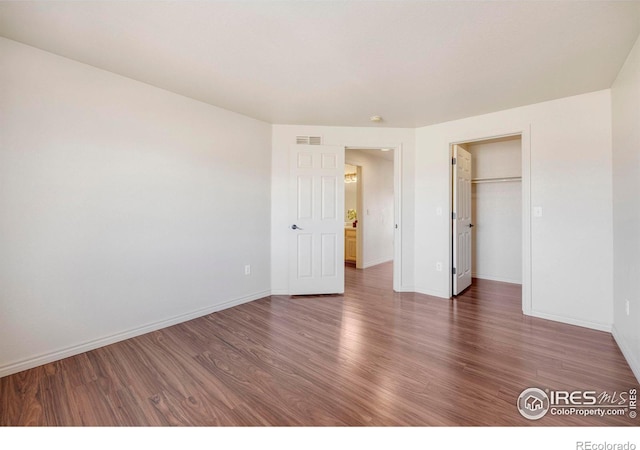 unfurnished bedroom featuring baseboards, a spacious closet, visible vents, and dark wood-type flooring